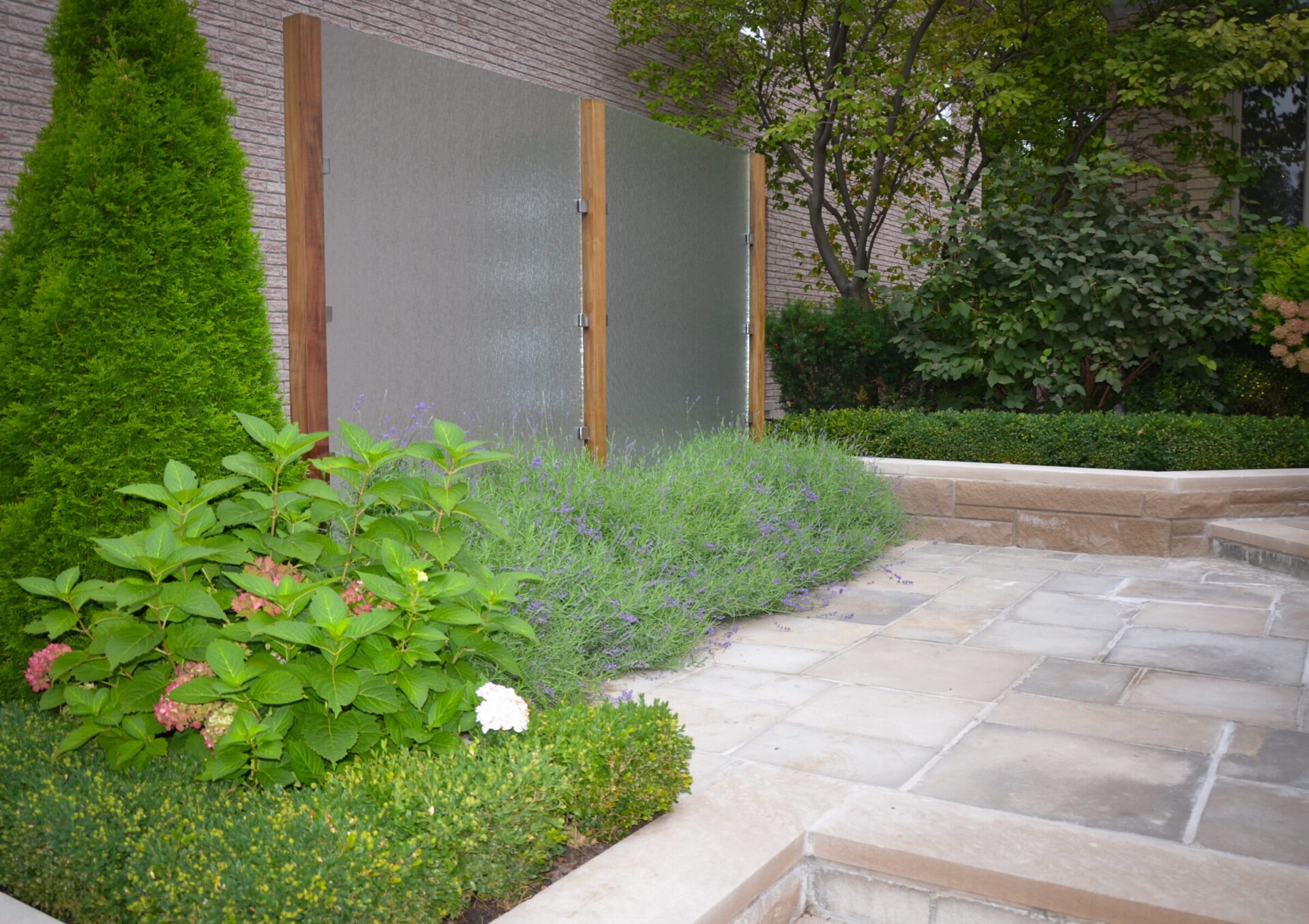 A serene garden scene featuring lush green plants and flowers, with a stone paved path and a frosted glass panel backdrop.