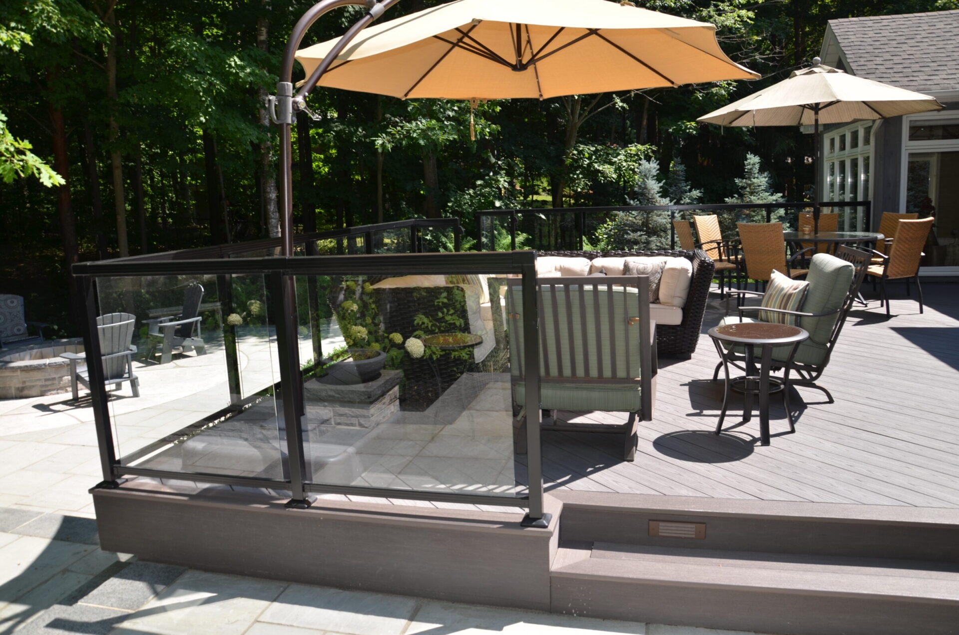 A spacious outdoor deck features seating, tables, and umbrellas surrounded by trees, creating a relaxing environment with a modern design.