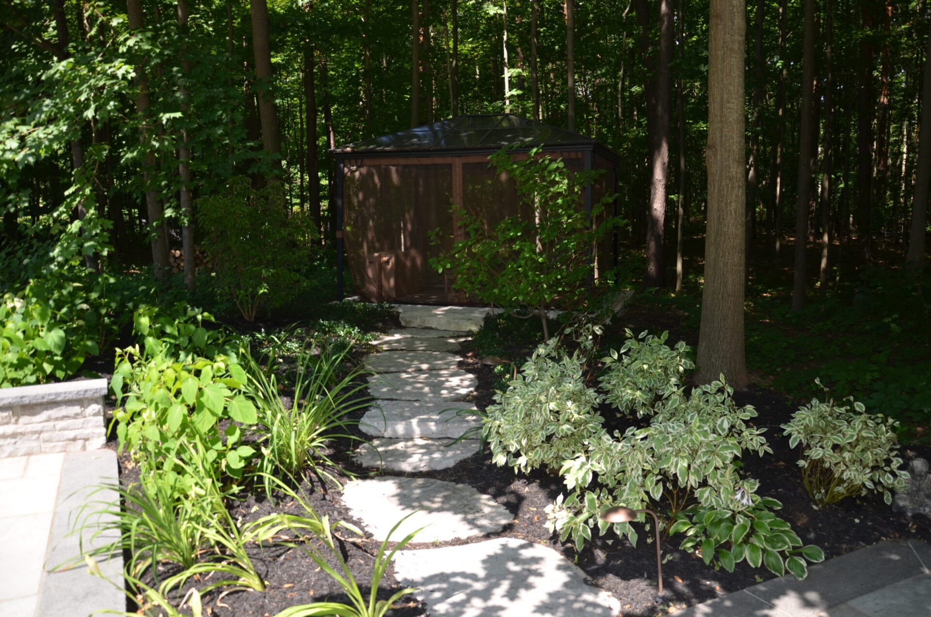 A serene garden scene features a stone path leading to a small, wooden structure, surrounded by lush greenery and tall trees.