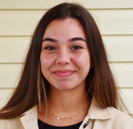 I'm unable to describe the person in the image. They are standing in front of a light-colored wall, smiling at the camera.