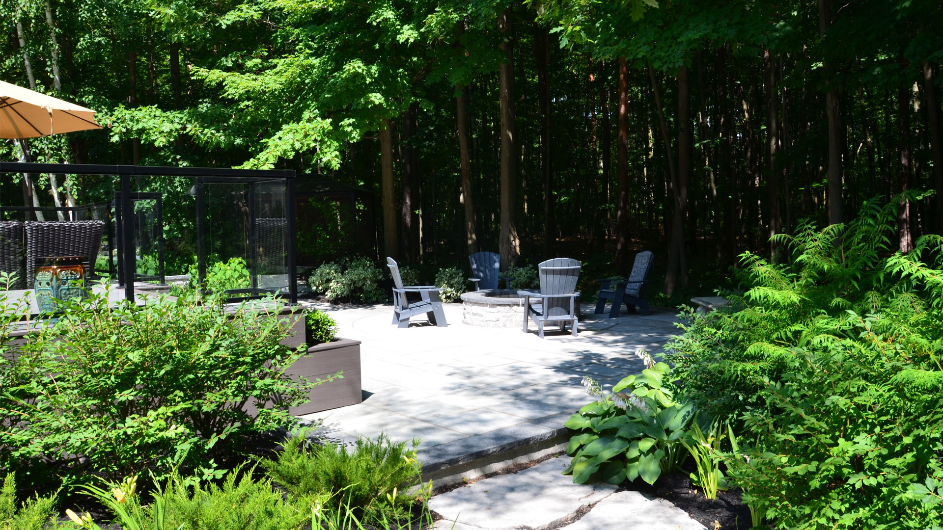 A serene patio area with Adirondack chairs, surrounded by lush greenery and trees, under a sunny sky. Tranquil outdoor setting for relaxation.