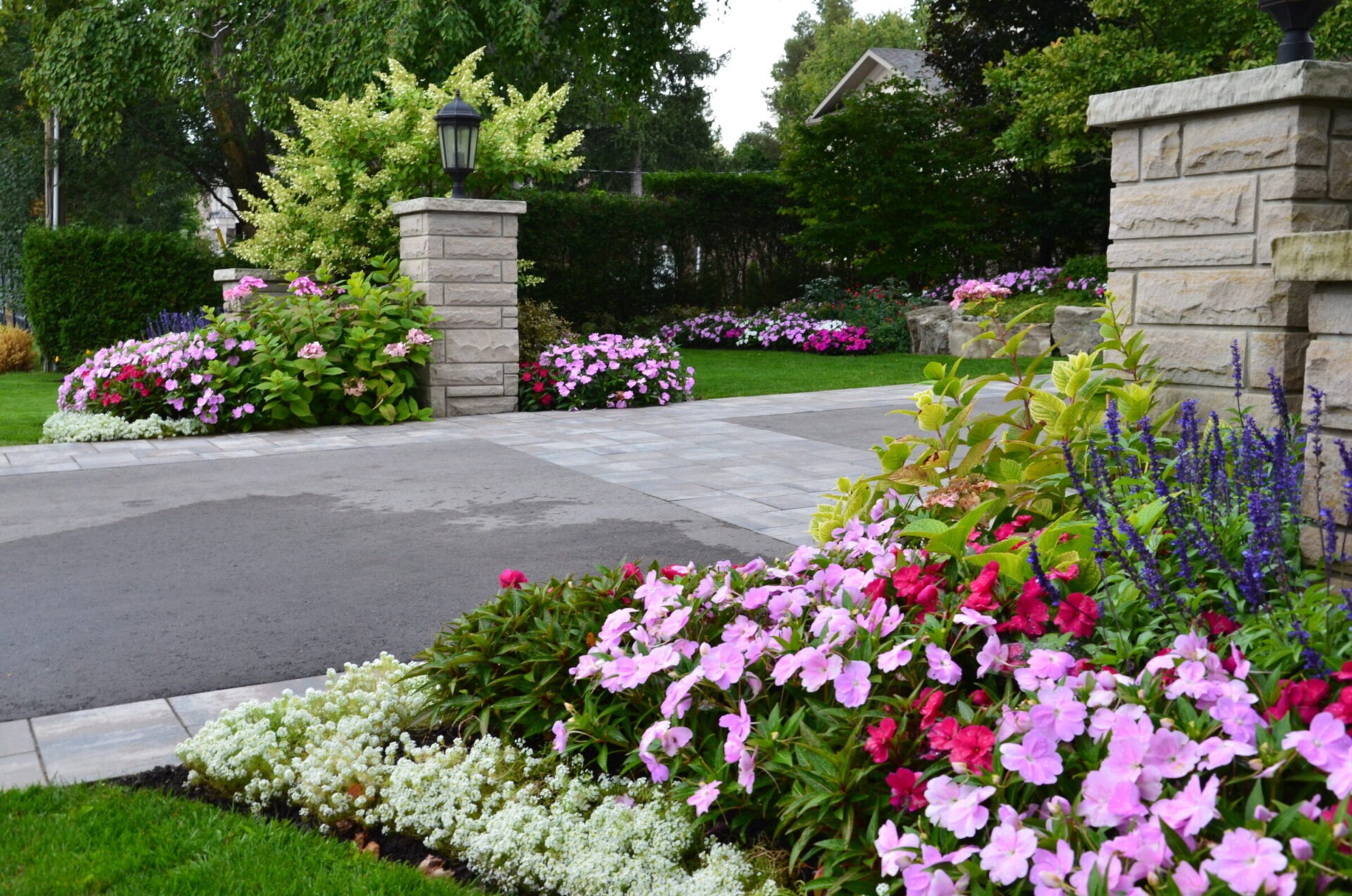 A beautifully landscaped garden with vibrant flowers, stone pathway, and pillars. Greenery surrounds the area, highlighting a serene and well-maintained environment.