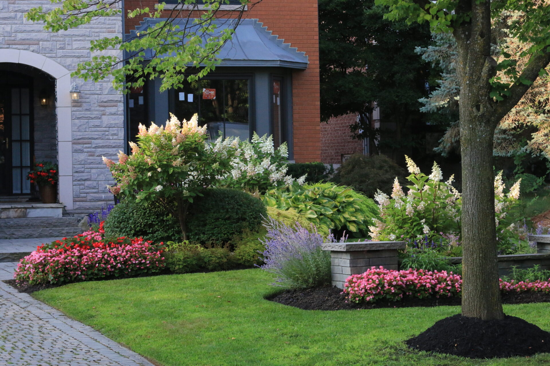 A picturesque garden features vibrant flowers, lush greenery, and a stone path leading to a brick and stone building entrance.