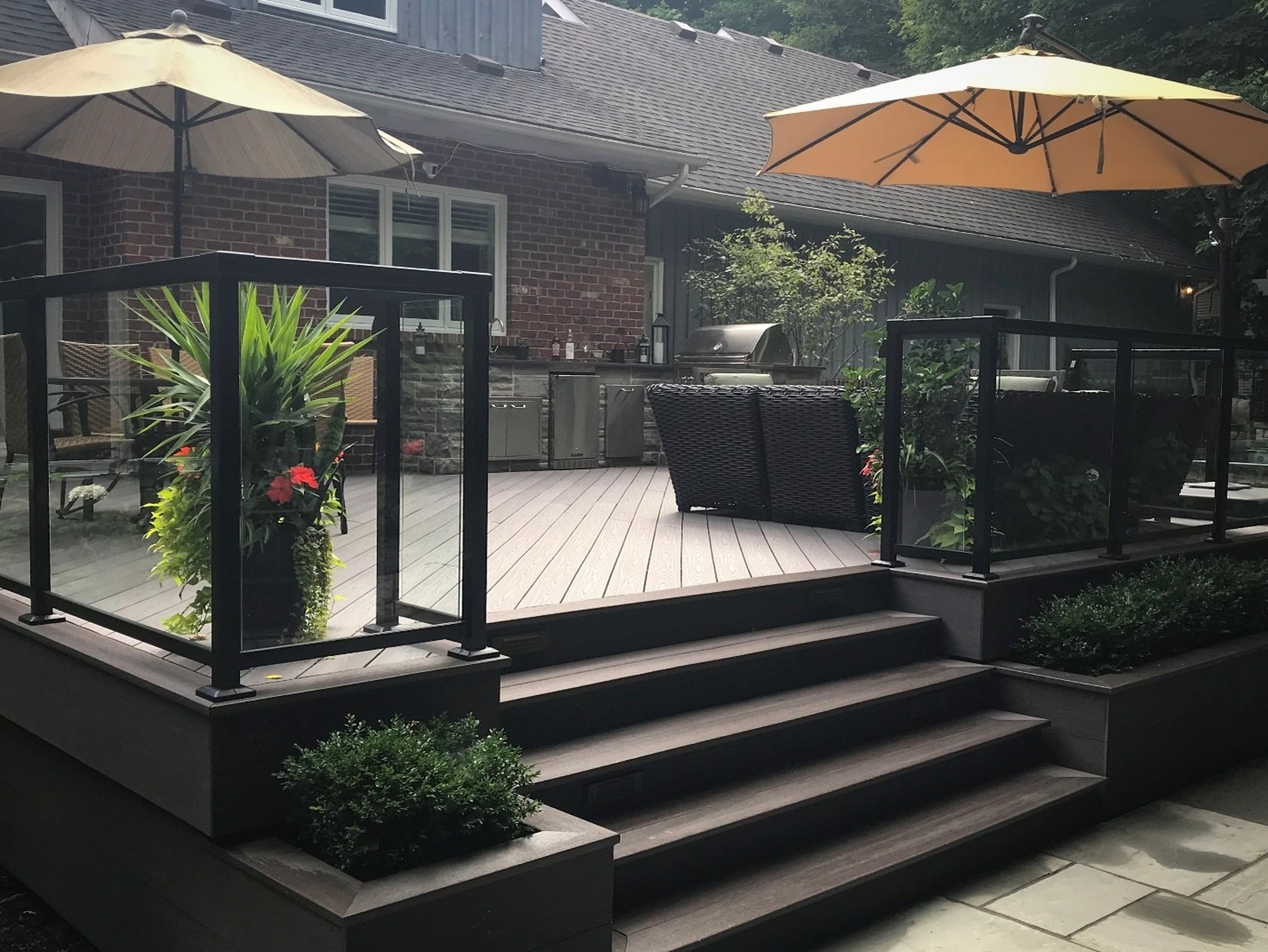A modern backyard patio with wooden decking, outdoor kitchen, shaded seating area, and decorative plants, providing a comfortable space for relaxation and entertaining.